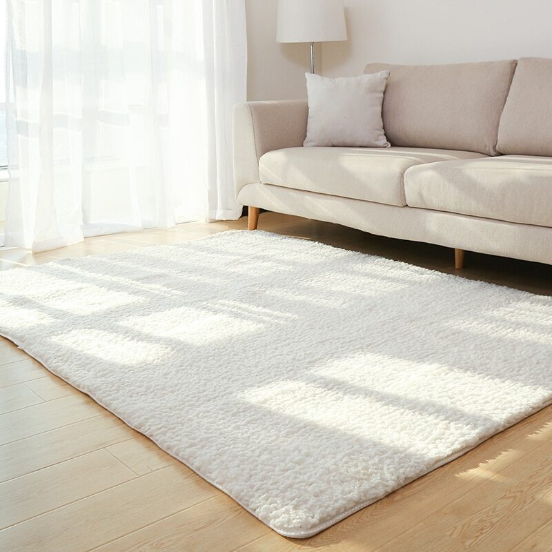 White rug on a wooden floor in a living room with a beige sofa and lamp.